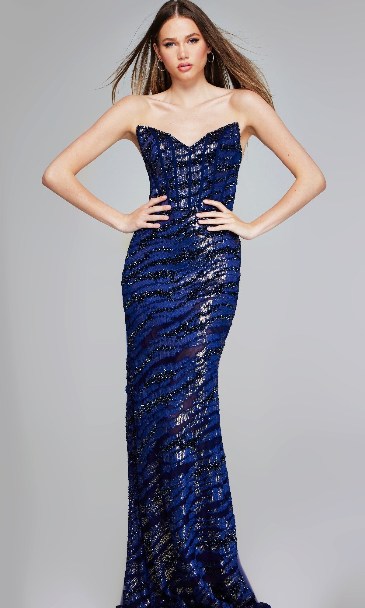 Model poses with hands on hips in the Jovani 40181 long formal dress, a strapless, form-fitting, floor-length evening gown in blue and black sequins, set against a plain background.